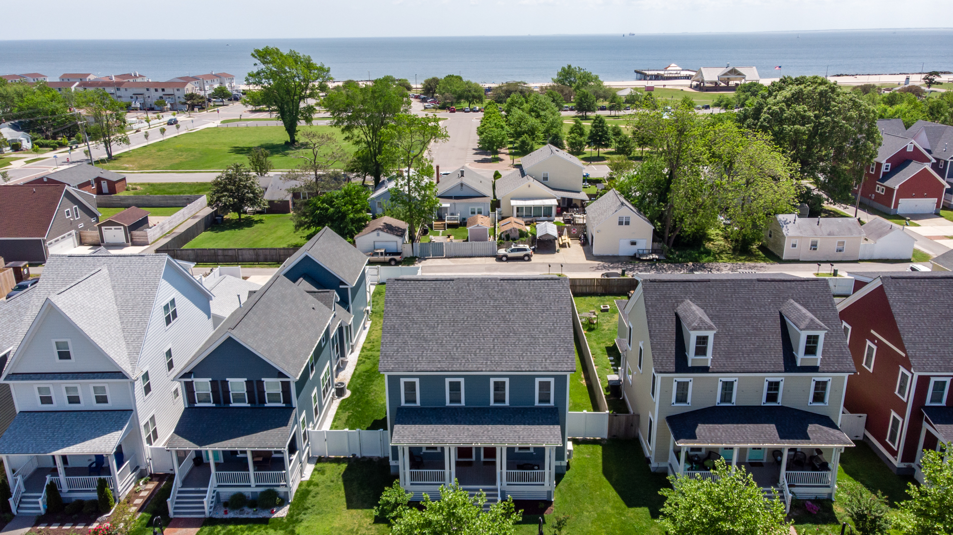 Aerial view of a blue home with a fenced backyard, located near the beach.